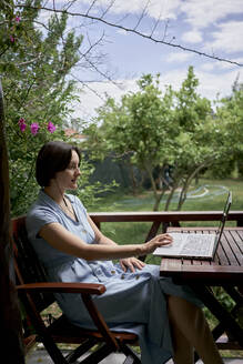 Freelancer using laptop sitting on chair on balcony - ANNF00005