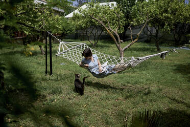 Frau auf Hängematte liegend mit Katze im Garten - ANNF00013