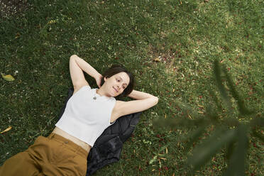 Frau mit Händen hinter dem Kopf entspannt im Gras - ANNF00020