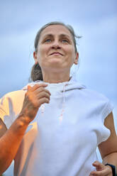 Entschlossene Frau mit Kapuzenshirt joggt vor dem Himmel - ZEDF04771