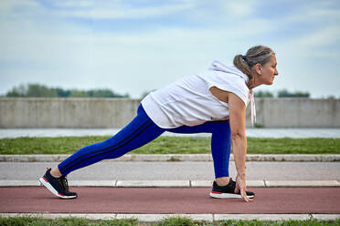 Mature woman preparing for run at sports track - ZEDF04774