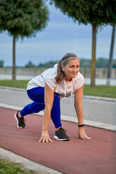 Smiling mature woman preparing for run at sports track - ZEDF04775