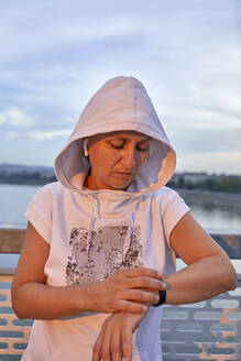 Frau mit Kapuzenshirt prüft Puls auf Smartwatch - ZEDF04784