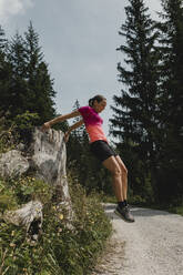 Hiker jumping from tree stump on footpath - DMGF00839