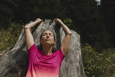 Woman with eyes closed leaning on tree stump in forest - DMGF00840