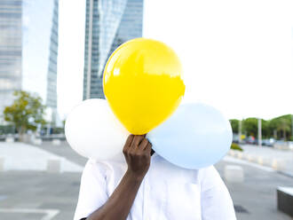 Junger Mann hält sich bunte Luftballons vor das Gesicht auf dem Fußweg - AMRF00087