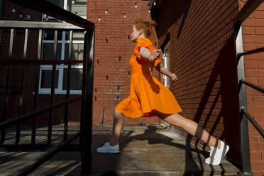 Frau in orangefarbenem Kleid beim Aufwärmen an einem sonnigen Tag - LLUF00844