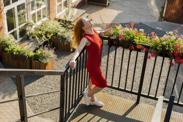 Woman wearing red dress with eyes closed leaning on railing - LLUF00862
