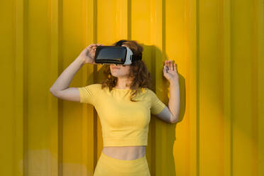 Woman wearing virtual reality simulator in front of yellow wall - LLUF00885