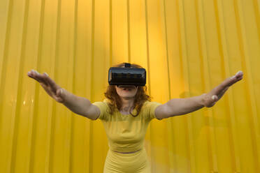 Woman wearing virtual reality simulator bending over in front of yellow wall - LLUF00888