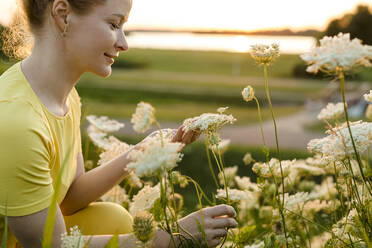 Lächelnde Frau mit Blick auf weiße Wildblumen - LLUF00893