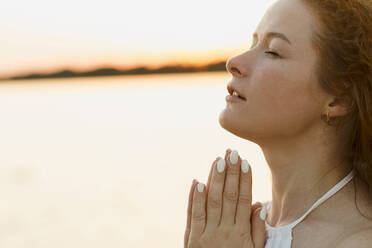 Beautiful woman with hands clasped at sunset - LLUF00895