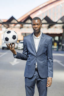 Junger Geschäftsmann mit Fußball auf einem Parkplatz an einem sonnigen Tag - IFRF01738