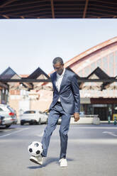 Young businessman playing with soccer ball at parking lot on sunny day - IFRF01740