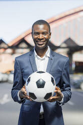 Happy young businessman with soccer ball standing at parking lot - IFRF01744