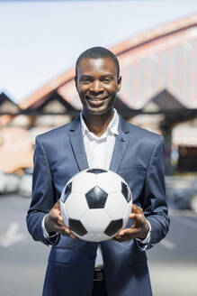 Glücklicher junger Geschäftsmann mit Fußball auf einem Parkplatz - IFRF01744