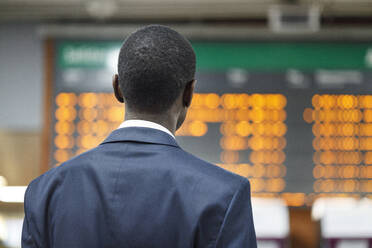 Businessman looking at departure board at railroad station - IFRF01751