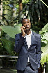 Businessman talking on smart phone in front of plants - IFRF01757