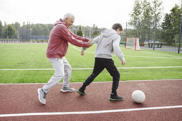 Glücklicher Großvater mit fußballspielendem Jungen auf einem Sportplatz - EYAF02171