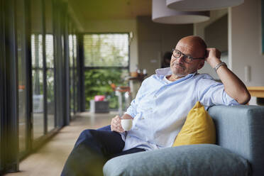 Älterer Mann im Ruhestand mit Kaffeetasse, der zu Hause auf dem Sofa sitzt - RBF08901