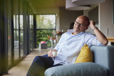 Retired senior man with coffee cup sitting on sofa at home - RBF08901