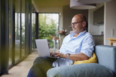 Man using laptop sitting on sofa at home - RBF08902