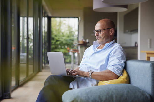 Mann mit Laptop auf dem Sofa zu Hause sitzend - RBF08902