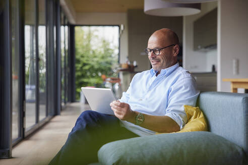 Lächelnder Mann mit Tablet-PC auf dem Sofa zu Hause - RBF08906
