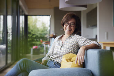 Happy senior woman sitting on sofa at home - RBF08911