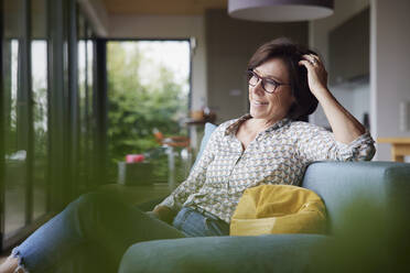 Thoughtful woman with hand in hair sitting on sofa at home - RBF08914