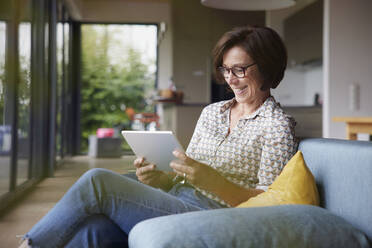 Zufriedene ältere Frau mit Tablet-PC auf dem Sofa zu Hause - RBF08918