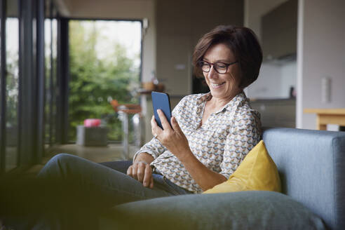 Glückliche ältere Frau, die zu Hause ein Smartphone benutzt - RBF08921