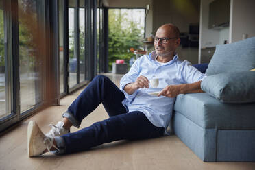 Lächelnder Mann mit Kaffeetasse, der zu Hause auf dem Sofa sitzt - RBF08926