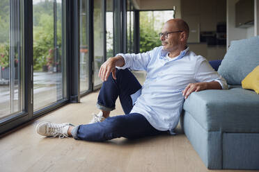 Thoughtful senior man sitting by sofa at home - RBF08930