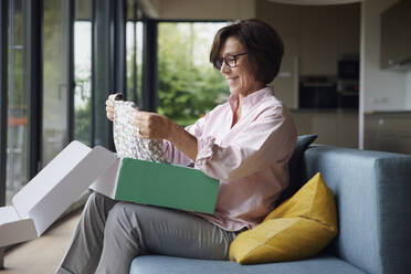 Glückliche Frau beim Auspacken des zu Hause erhaltenen Pakets - RBF08940