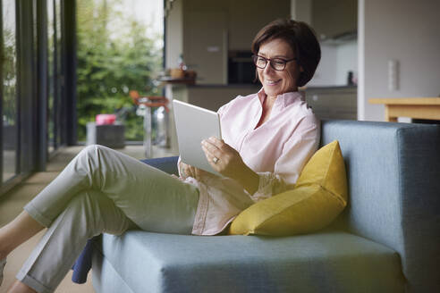 Glückliche Frau mit Tablet-PC zu Hause sitzend - RBF08941