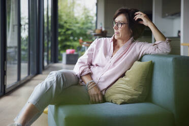 Thoughtful woman wearing eyeglasses sitting on sofa at home - RBF08945