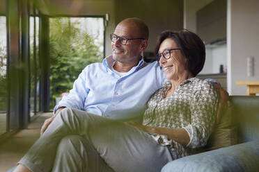 Glücklicher älterer Mann und Frau sitzen auf dem Sofa zu Hause - RBF08949