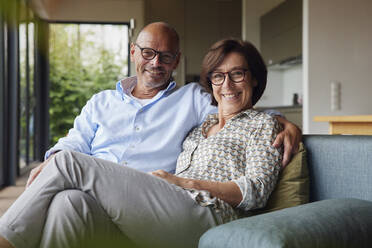 Happy senior couple wearing eyeglasses sitting together at home - RBF08952