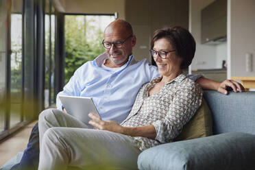 Happy senior woman with man using tablet PC on sofa at home - RBF08954