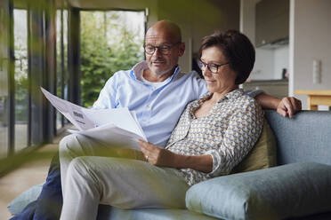 Lächelnder Mann mit Frau beim Lesen von Dokumenten zu Hause - RBF08955