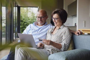 Happy couple making payment through credit card on laptop at home - RBF08956