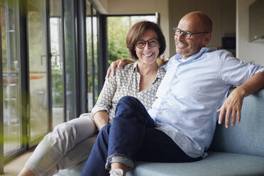 Cheerful senior couple sitting on sofa together at home - RBF08963