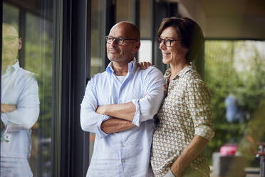 Senior woman with man looking out through window at home - RBF08970