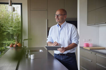 Lächelnder älterer Mann mit Tablet-PC an der Kücheninsel zu Hause - RBF08986