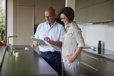 Happy woman with man using tablet PC standing in kitchen at home - RBF08987