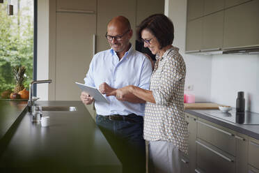 Happy senior couple using tablet PC in kitchen at home - RBF08988