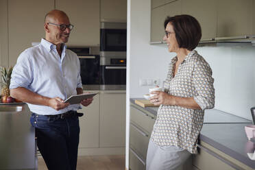 Happy senior man holding tablet PC standing with woman in kitchen at home - RBF08989