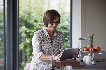 Lächelnde ältere Frau mit Tablet-PC an der Kücheninsel - RBF09004