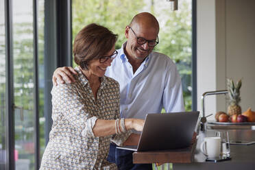 Glückliches älteres Paar, das zu Hause gemeinsam einen Laptop benutzt - RBF09008